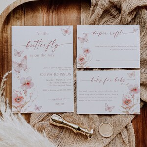 May include: A baby shower invitation with a pink and white floral design and butterflies. The invitation says "A little butterfly is on the way" and includes the name Olivia Johnson. There are also cards for a diaper raffle and a book request for the baby.