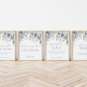 May include: Four printable signs with a watercolor floral design in shades of blue and white. The signs read "Measure the Baby Bump", "Please Sign the Guestbook", "Pacifier Hunt", and "Flower Bar".