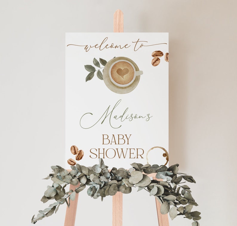May include: Welcome to Madison's Baby Shower sign with a watercolor illustration of a coffee cup with a heart design and coffee beans. The sign is on a wooden easel with greenery.