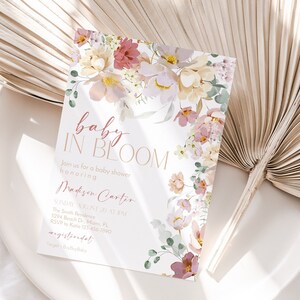 May include: A baby shower invitation featuring a floral design. The invitation reads "baby in bloom" and includes the name "Madison Carter". The invitation also includes the date, time, and location of the shower.