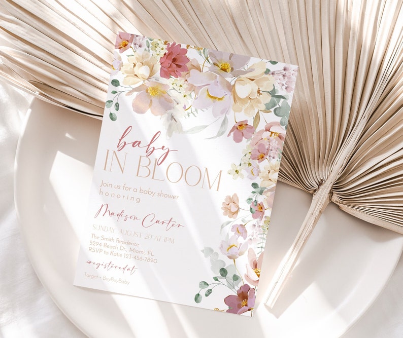 May include: A baby shower invitation featuring a floral design. The invitation reads "baby in bloom" and includes the name "Madison Carter". The invitation also includes the date, time, and location of the shower.