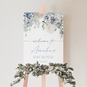 May include: A welcome sign for a baby shower with a watercolor floral design in shades of blue and white. The sign says "Welcome to Amelia's Baby Shower 06.21.2023".