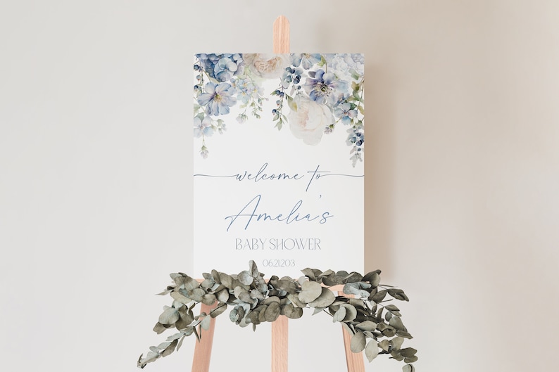 May include: A welcome sign for a baby shower with a watercolor floral design in shades of blue and white. The sign says "Welcome to Amelia's Baby Shower 06.21.2023".