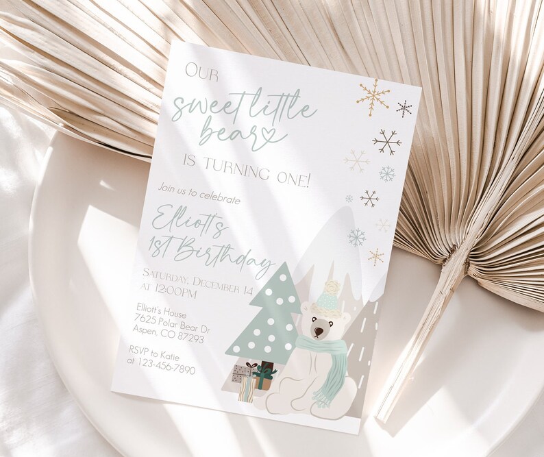 May include: A light-colored invitation card with the text "Our sweet little bear is turning one!" and details for a first birthday party. The design includes a polar bear, a Christmas tree, snowflakes, and mountains.
