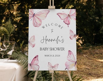 May include: A white welcome sign with pink watercolor butterflies and the text "Welcome to Hannah's Baby Shower March 21, 2024".