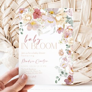 May include: A baby shower invitation featuring a floral design in shades of pink, white, and green. The text reads "baby in bloom" and includes the name "Madison Carter".