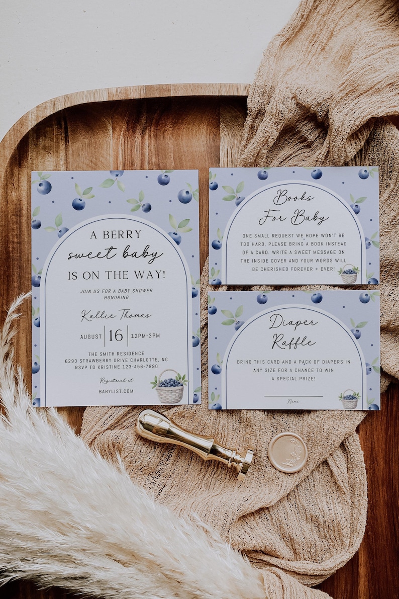 May include: A blue and white baby shower invitation with a blueberry theme. The invitation includes the text "A Berry Sweet Baby Is On The Way!" and details for the shower, including the date, time, location, and RSVP information. There are also two additional cards for a book and diaper raffle.