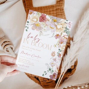 May include: A baby shower invitation featuring a floral design. The invitation reads "baby in bloom" and includes the name "Madison Carter". The invitation is decorated with watercolour flowers in shades of pink, yellow, and green.