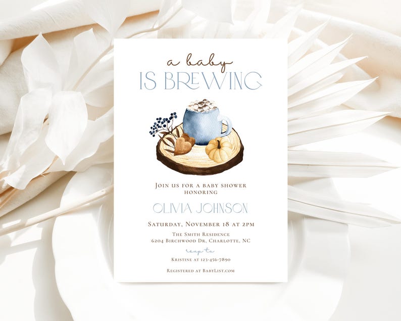 Op de afbeelding: Een witte rechthoekige uitnodigingskaart voor een babyshower met de tekst a baby IS BREWING, OLIVIA JOHNSON en evenementdetails. Het ontwerp bevat een aquarelillustratie van een blauwe mok, een kleine pompoen en bessen op een houten schijf.