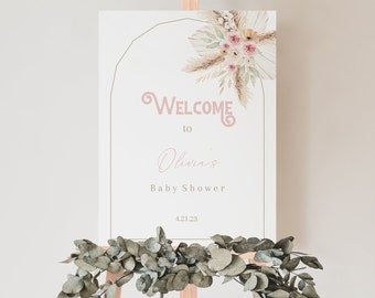 May include: A welcome sign for a baby shower with a floral design featuring dried pampas grass and pink roses. The sign reads "Welcome to Olivia's Baby Shower 4.21.23".