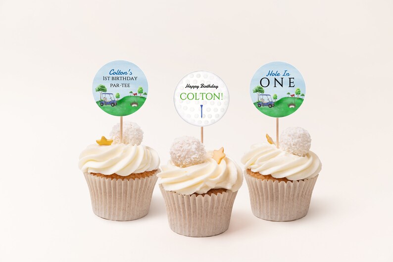 May include: Three cupcakes decorated with golf-themed toppers. The toppers feature a golf buggy, golf balls, and the text "Colton's 1st Birthday Par-Tee", "Happy Birthday Colton!" and "Hole In One".
