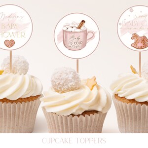 May include: Three cupcake toppers with pink and white designs. The first topper says "Madison's Baby Shower" with a pink heart. The second topper has a pink mug with marshmallows and a cinnamon stick, and says "Baby it's cold outside". The third topper has a pink rocking horse and says "A sweet Baby Girl is on her way".