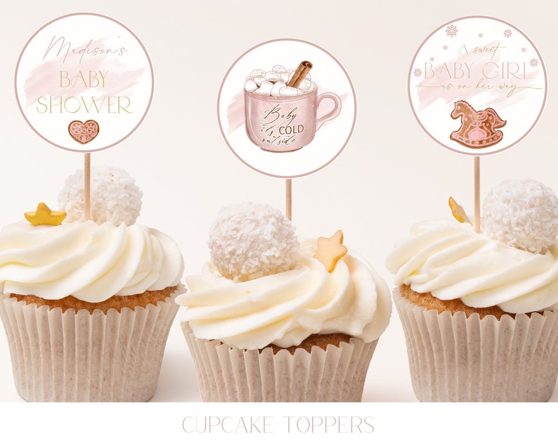 May include: Three cupcake toppers with pink and white designs. The first topper says "Madison's Baby Shower" with a pink heart. The second topper has a pink mug with marshmallows and a cinnamon stick, and says "Baby it's cold outside". The third topper has a pink rocking horse and says "A sweet Baby Girl is on her way".