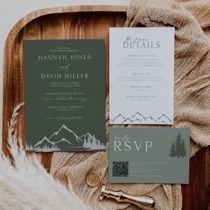 May include: A wedding invitation suite featuring a dark green main card with white mountain and forest graphics, a white details card with mountain line art, and a sage green RSVP card with a QR code, all accented by a gold wax seal stamp.