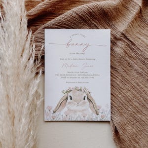 May include: A baby shower invitation with a cute illustration of a bunny wearing a flower crown. The invitation reads "a sweet little bunny is on the way!" and includes the name "Medison Jence", the date "March 18 at 2:00 pm", the location "The Smith Residence | 6293 Birchwood Drive", and the RSVP information.