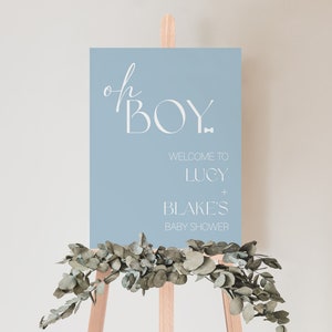May include: A light blue baby shower sign with white text that reads "oh boy" in a script font and "Welcome to Lucy + Blake's Baby Shower" in a sans-serif font.