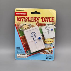 May include: A packaged Mystery Date Game keychain. The white keychain features a door design with a blue question mark and a blue button. The packaging reads "Mystery Date Game Keychain" and "Really Works!"