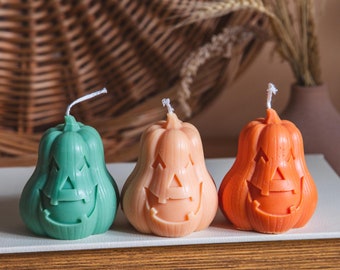 Könnte beinhalten: Drei Halloween-Kerzen in Form von Kürbissen mit geschnitzten Jack-o'-Lantern-Gesichtern. Die Kerzen sind grün, pfirsichfarben und orange.