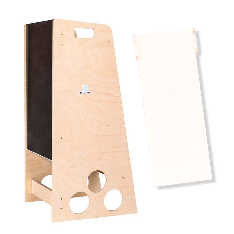 Puede incluir: Un taburete de madera con un panel de pizarra negra en la parte delantera. El taburete tiene un asa recortada en la parte superior y tres agujeros redondos en la parte inferior. El taburete est&aacute; etiquetado con "mami" en azul.