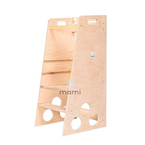 Puede incluir: Un taburete de madera con un pasamanos incorporado y compartimentos de almacenamiento. El taburete est&aacute; hecho de madera natural y tiene un acabado marr&oacute;n claro. El nombre de la marca "mami" est&aacute; impreso en el lateral del taburete.