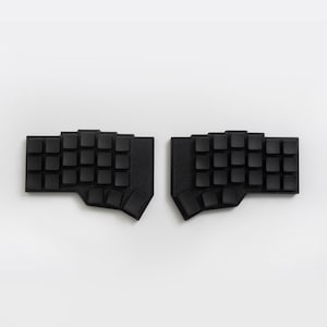 May include: A split ergonomic keyboard set consisting of two separate black units. Each unit features a contoured layout of blank, square keys arranged in a staggered grid pattern, designed for a two-handed typing configuration.