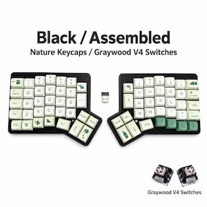 May include: A split ergonomic mechanical keyboard with black housing and off-white keycaps featuring green nature-themed icons. Text reads Black / Assembled Nature Keycaps / Graywood V4 Switches. Includes a small USB receiver and two Graywood V4 switches.