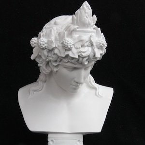 May include: White plaster bust of a person with a crown of leaves and berries. The bust is on a white pedestal.
