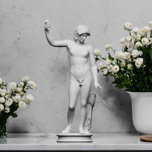 A small white 3D sculpture print of the Statue of Liberty is placed between two potted plants.