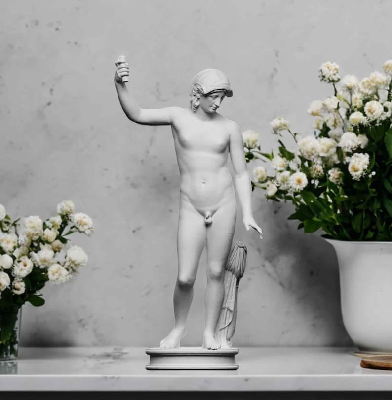 A small white 3D sculpture print of the Statue of Liberty is placed between two potted plants.