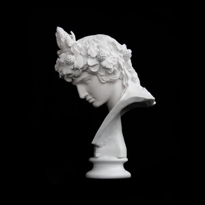 May include: White plaster bust of a person with a floral crown, the bust is on a white pedestal.