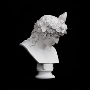 May include: White plaster bust of a woman with a wreath of leaves and berries on her head. The bust is on a pedestal.