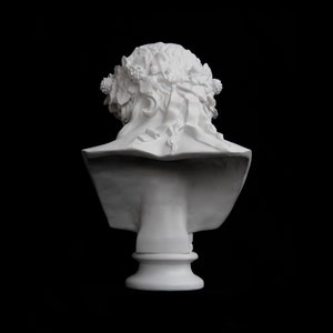 May include: White plaster bust of a woman with a floral crown, viewed from the back. The bust is on a pedestal.