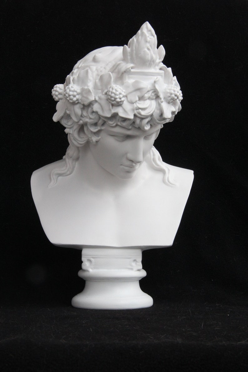 May include: White plaster bust of a person with a crown of leaves and berries. The bust is on a white pedestal.