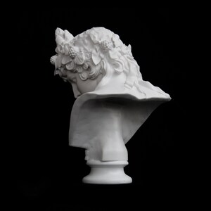 May include: White plaster bust of a woman with a crown of leaves and berries on her head. The bust is tilted to the side, and the woman's face is obscured by the crown.