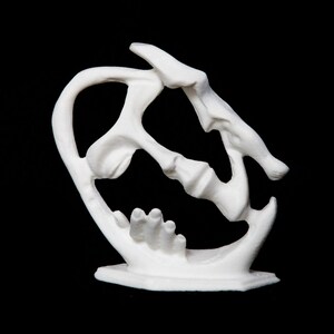 Puede incluir: Escultura de cerámica blanca de dos caras entrelazadas, creando un diseño único y abstracto. La escultura está sobre una pequeña base.
