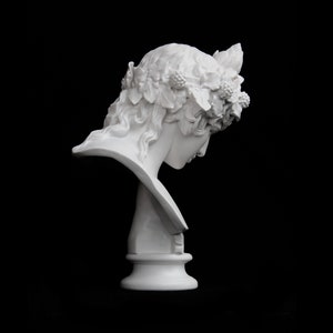 May include: White plaster bust of a woman with a wreath of leaves and berries on her head. The bust is on a pedestal and is angled to the side.