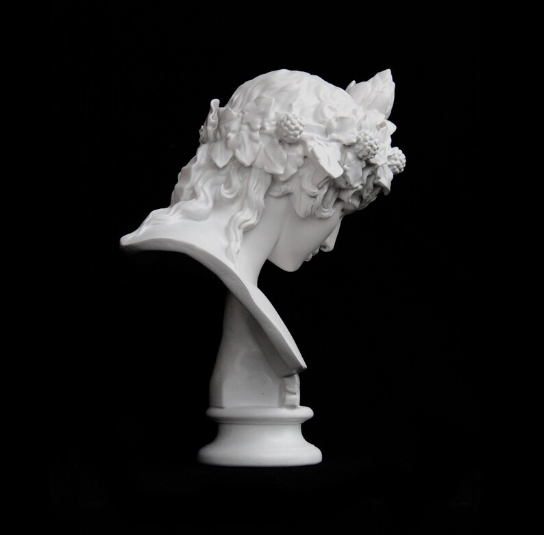 May include: White plaster bust of a woman with a wreath of leaves and berries on her head. The bust is on a pedestal and is angled to the side.
