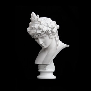 May include: White plaster bust of a person wearing a wreath of leaves and berries. The bust is on a white pedestal.