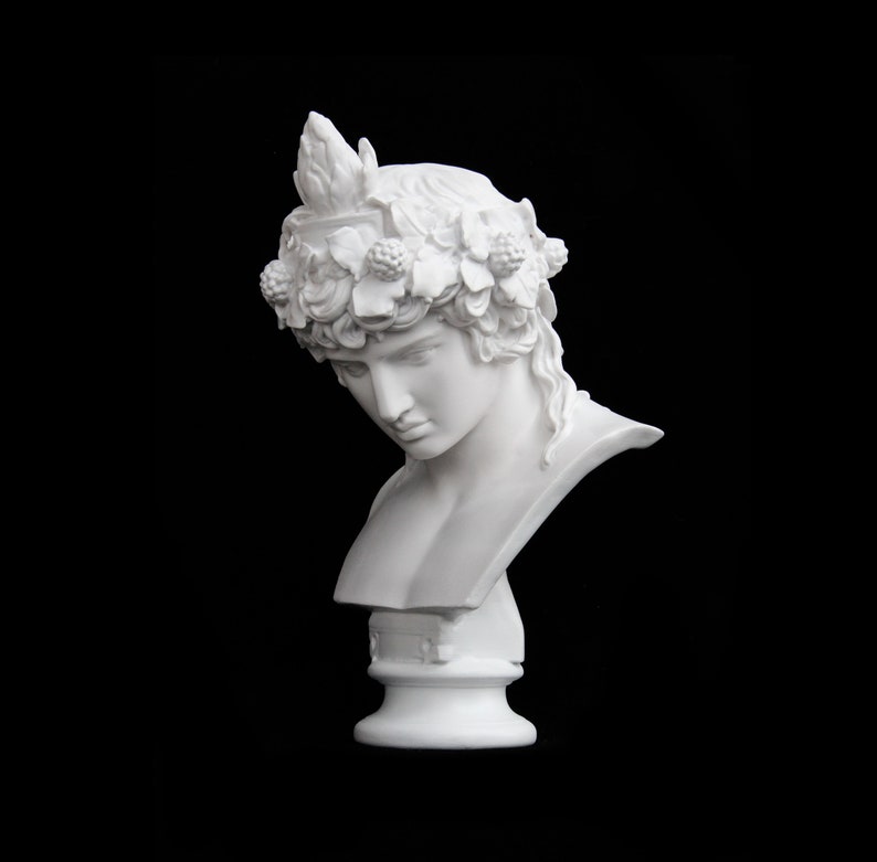 May include: White plaster bust of a person wearing a wreath of leaves and berries. The bust is on a white pedestal.