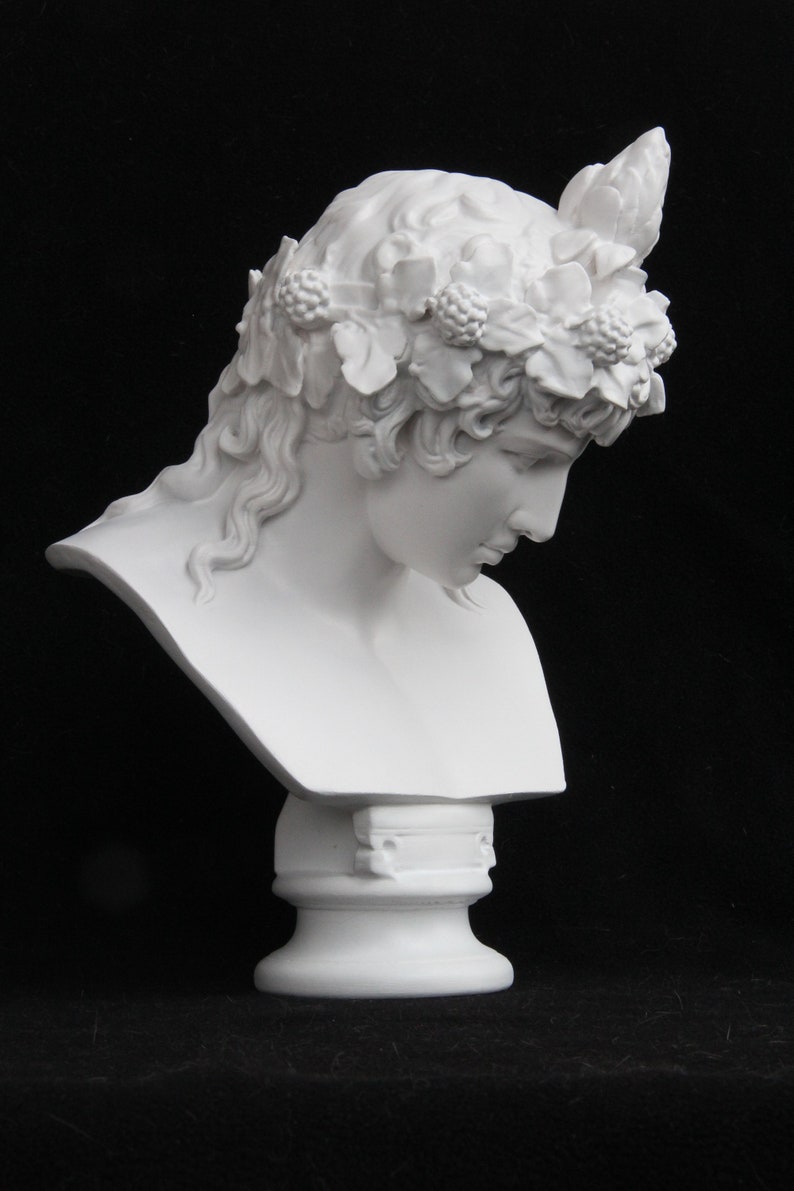 May include: White plaster bust of a person with a floral crown. The bust is on a white pedestal.