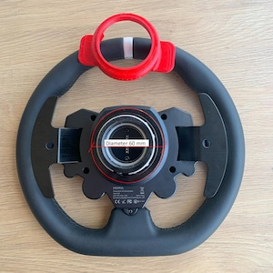 Op de afbeelding: Een zwart stuur met een rode bevestiging. Het wiel heeft een diameter van 60 mm. Het wiel is zwart met een lederachtige grip. De rode bevestiging heeft een witte streep.