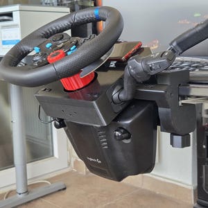 May include: Black and gray racing wheel and gearshift setup. The wheel has a black leather grip with blue accents and a red center. The gearshift is mounted to a desk with a black clamp.
