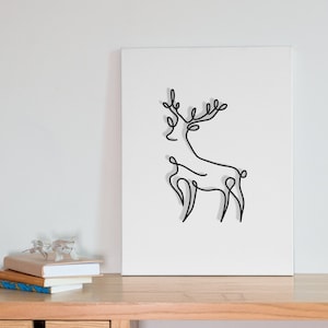以下が含まれることがあります： 白いキャンバスに、角のある鹿のミニマルな線画が描かれています。明るい木製の机に、引き出しが2つ付いています。机の上には本が積み重ねられています。
