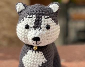 May include: A crocheted gray and white husky dog plush toy with black eyes and a gold bell on its collar.