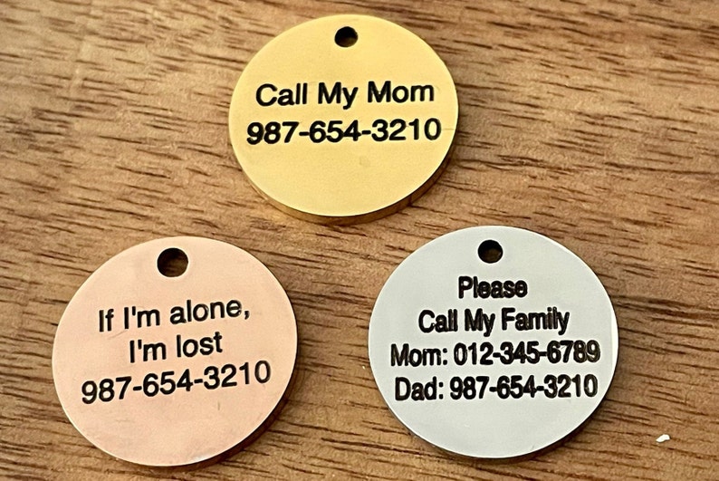 May include: Three round metal pet ID tags with black engraved text. The gold tag reads "Call My Mom 987-654-3210". The copper tag reads "If I'm alone, I'm lost 987-654-3210". The silver tag reads "Please Call My Family Mom: 012-345-6789 Dad: 987-654-3210".