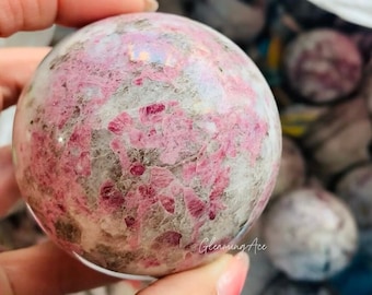 May include: A pink and white sphere with a swirling pattern of pink and white crystals. The sphere is made of natural stone and has a smooth, polished surface.