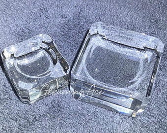 May include: Two clear glass ring display stands, one larger than the other, on a gray fabric surface.