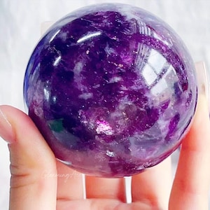 Peut inclure: Une grande sphère d'améthyste violette avec un motif tourbillonnant et nuageux. La sphère est lisse et polie, et elle reflète magnifiquement la lumière.
