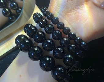 May include: Four black beaded bracelets stacked on a person's wrist. The bracelets are made of round, smooth beads.