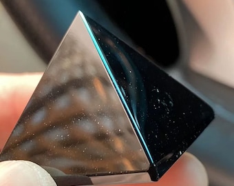 Könnte beinhalten: Eine schwarze Obsidianpyramide mit einer glatten, polierten Oberfläche. Die Pyramide reflektiert das Licht und erzeugt einen schimmernden Effekt.